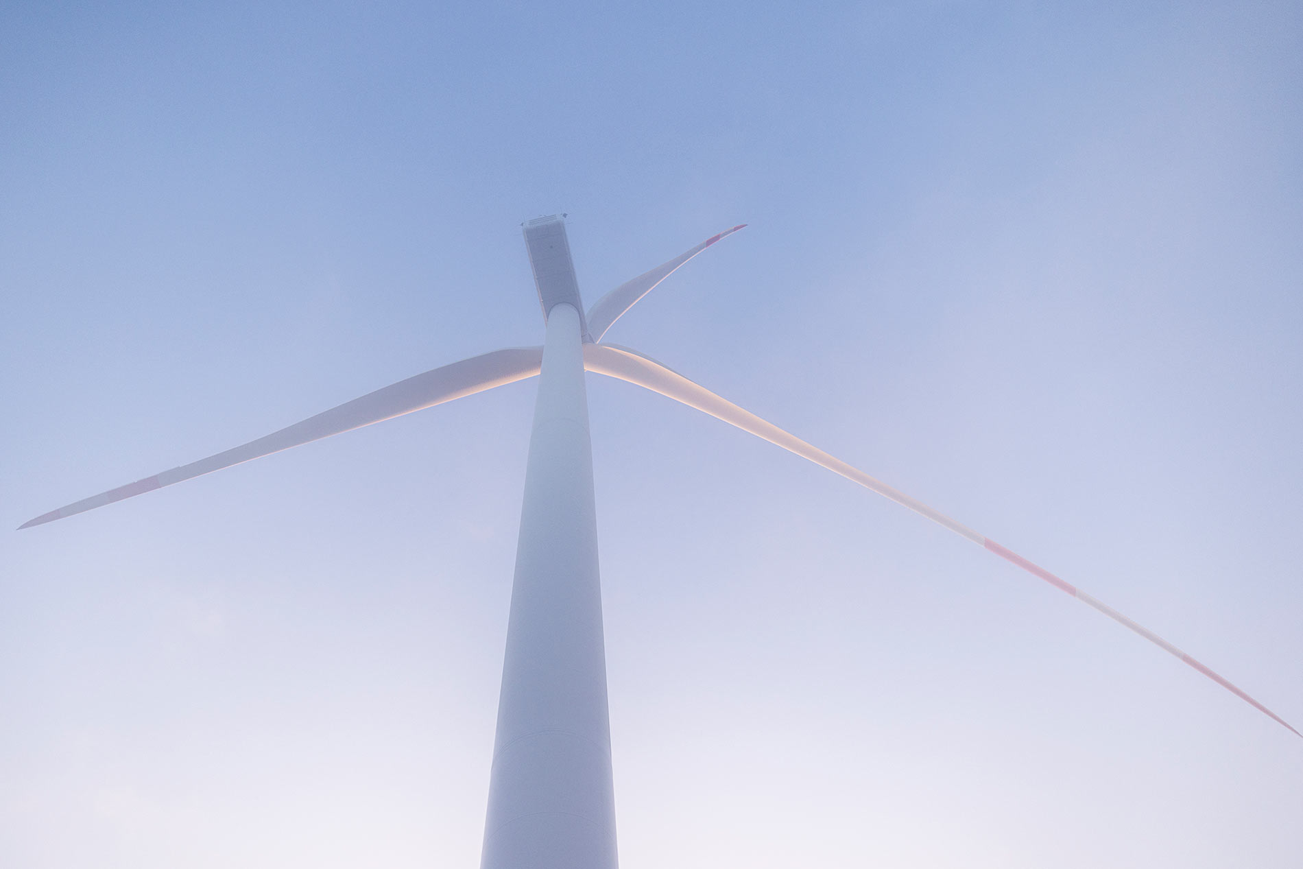 Windkraftrad vor blauem Himmel und aufgehender Sonne