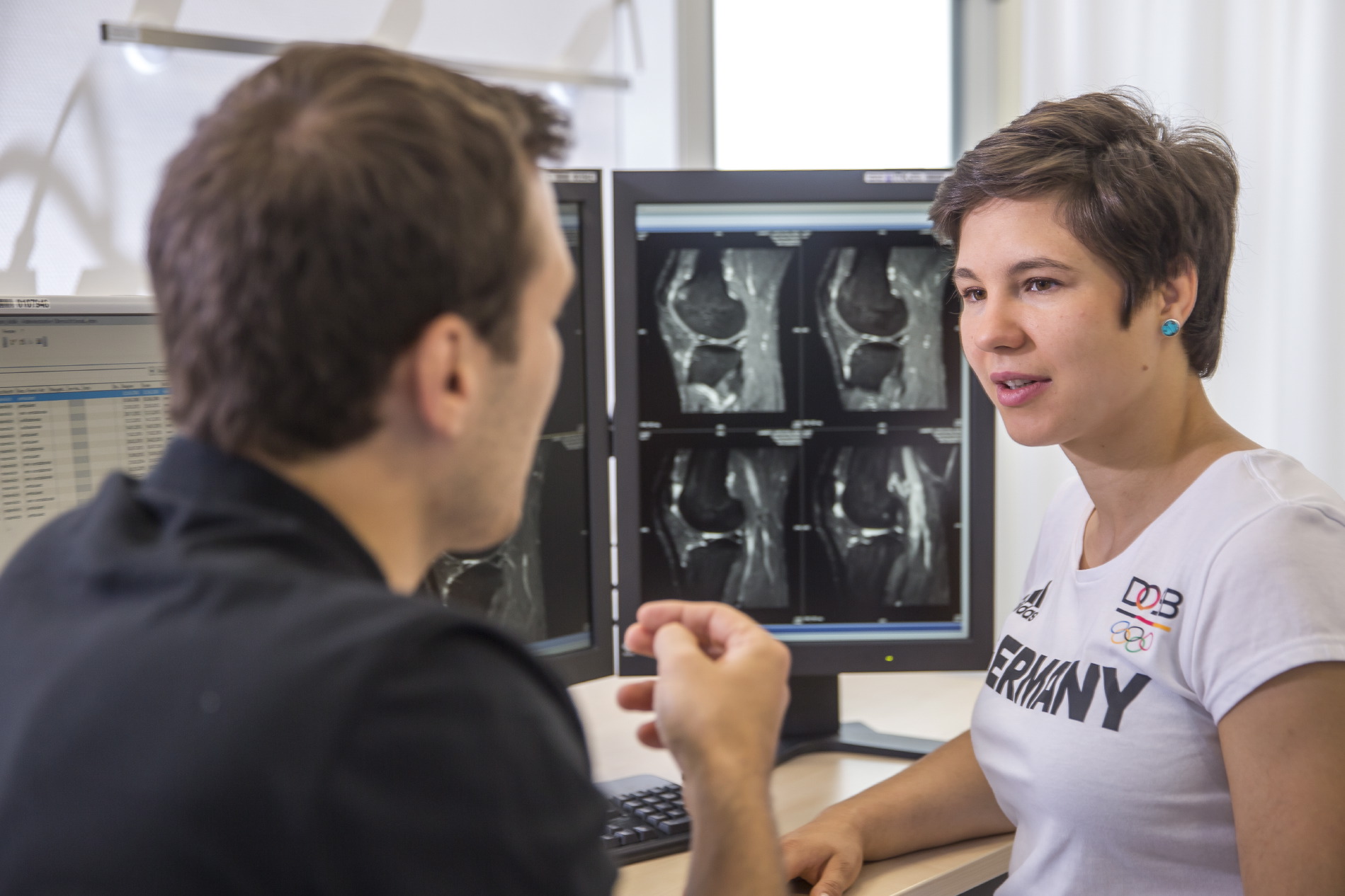 Ein Sportarzt berät eine Patientin an Röntgenbildern