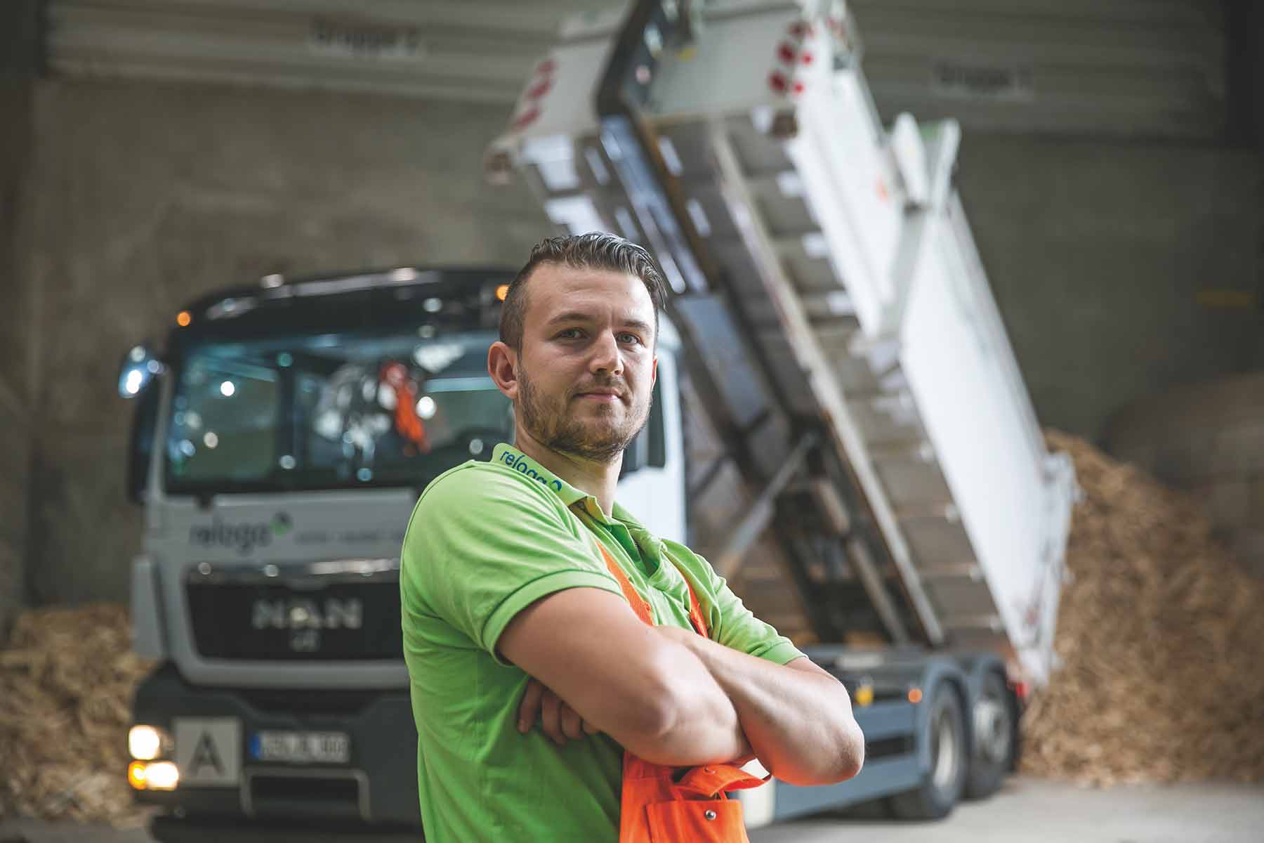 Ein Auszubildender steht mit verschränkten Armen vor einem Fahrzeug